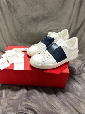 Valentino Garavani sneakers vit/blå - Byter gärna ett par ett par Valentino Garavani sneakers i vitt skinn med bred marinblå detalj över snörningen. Skorna har rund tå, platt sula och ikoniska nitar baktill. Klassisk och stilren modell med logga på plösen. Perfekta för dig som gillar exklusiva sneakers. Mot ett par loubs med spikar har tröttnat på dom jag har 