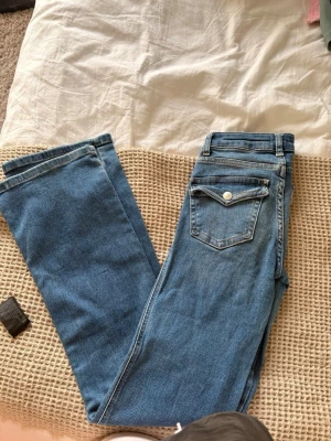 Blå jeansbyxor med ficklock - Säljer ett par klassiska blå jeansbyxor från 157 med raka ben och snygga ficklock bak med knappdetalj. Jeansen har normal passform och är tillverkade i slitstarkt bomullsmaterial. Perfekta till vardags och matchas lätt med det mesta.