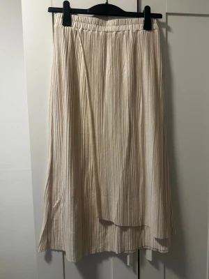 Plisserad beige långkjol från & Other Stories - Säljer en plisserad beige långkjol från & Other Stories i storlek S. Kjolen har elastisk midja och ett mjukt, flowy tyg som ger en snygg siluett. Perfekt för dig som gillar stilrena och enkla plagg med lite extra detalj tack vare de fina vecken.