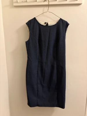 Mörkblå prickig ärmlös klänning - Snygg mörkblå kortklänning med små vita prickar och klassisk rak passform. Klänningen är ärmlös och har rund halsringning samt dragkedja i ryggen. Perfekt för dig som gillar stilrena och tidlösa plagg.