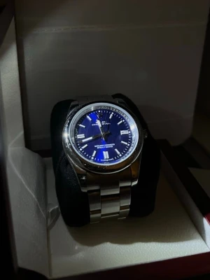 Klassisk klocka  - Denna klocka har en stabil vikt, är tillverkad i rostfritt stål och har en mekanisk rörelse som fungerar smidigt och håller tiden pålitligt. Perfekt för dig som vill ha en stilren och klassisk klocka i eftertraktad storlek. Extra länkar ingår. Storlek 39 mm, mörkblå sunburst-tavla med kromade index, repsäkert safirglas, Oyster-länk i stål, visar timmar, minuter och sekunder, vattentät 100 m.