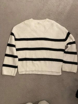 randig stickad tröja - Säljer en vit stickad tröja med svarta ränder. Tröjan har en avslappnad passform, rund halsringning och långa ärmar.