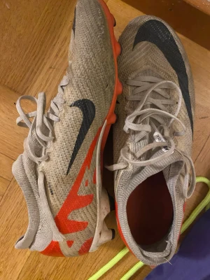 Nike fotbollsskor i beige och orange - Säljer ett par Nike fotbollsskor. Skorna har använts och är rätt slitna men håller fortfarande hög kvalité 
