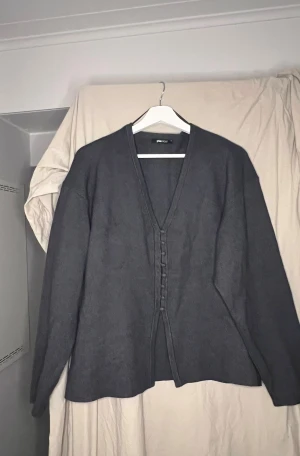 Mörkgrå kofta från Gina Tricot - Säljer en stilren mörkgrå kofta från Gina Tricot i storlek XL. Koftan har v-ringad hals, långa ärmar och knappar framtill. Materialet är mjukt och stickat, perfekt för lager-på-lager under höst och vinter. Enkel att matcha med jeans eller kjol.