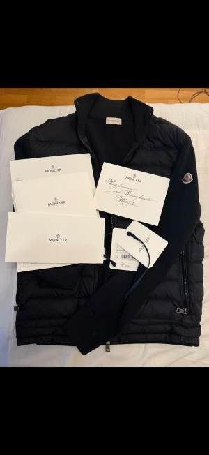 Moncler Tricot Cardigan - Säljer min välvårdade Moncler Tricot Cardigan som jag inte använder längre. Har tröttnat på den och slutat med märkeskläder. Den är självklart äkta, tags, kvitto och allt finns. Storlek: M. Kan även fraktas och tar endast Swish! Kör utanför denna appen! Svart pufferjacka från Moncler med quiltad framsida och stickade ärmar. Jackan har hög krage, dragkedja framtill och två sidofickor med dragkedja. Moncler-logga på vänster ärm. Materialmix av polyester och stickad ull ger en modern look.