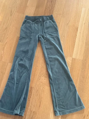 Gröna Juicy Couture XXS - Snygga gröna Juicy Couture-byxor i mjuk, sammetsliknande velour! Byxorna är i fint skick och supersköna att bära. De har fickor baktill och ett snöre i midjan, där ena metall-/dekordelen saknas – inget som påverkar funktionen