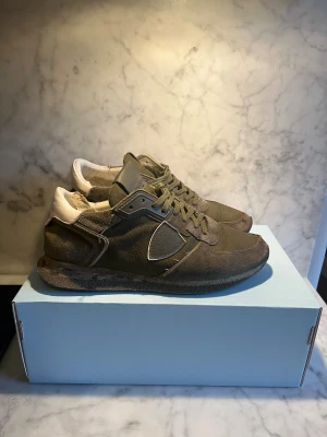 Philippe Model trainers  gröna sneakers herr - Snygga sneakers från Philippe Model i olivgrönt med vita detaljer på hälen. Skorna har snörning, rund tå och en cool camouflagemönstrad sula. Materialmix av mocka och textil ger en schysst streetkänsla. Perfekt för dig som gillar unika och trendiga sneakers. Hör av vid fler bilder eller frågor !!