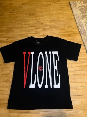 Svart VLONE t-shirt med draktryck - Svart t-shirt från VLONE i bomull med stor vit och röd VLONE-logga på framsidan och en fet röd drake tryckt över ett V på ryggen. Klassisk rund hals och korta ärmar. Perfekt för dig som gillar streetwear och vill sticka ut med coola prints.