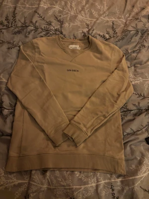 Beige sweatshirt från Les Deux - Snygg beige sweatshirt från Les Deux med diskret svart text på bröstet. Tröjan har rund hals, ribbade muddar vid ärmslut och nederkant samt långärmad passform. Storlek S. Tröjan är använd få tal gånger.