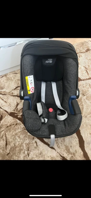 Britax Römer Baby-Safe i-Size - Britax Römer Baby-Safe i-Size babyskydd i snyggt grått tyg. Säker och bekväm med justerbar sele och bärhandtag. Inga synliga defekter eller slitage, ser ut att vara i mycket gott skick. Passar nyfödda och små barn, enkel att montera i bilen.