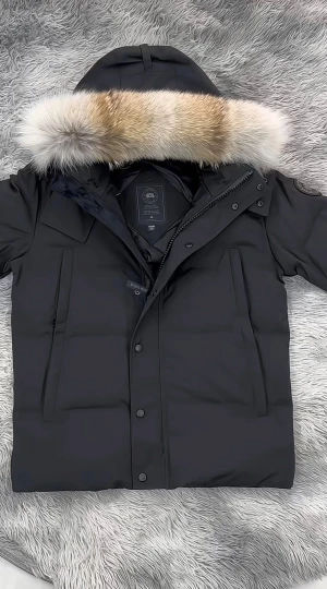 Svart Canada Goose dunjacka med päls - Säljer en svart dunjacka från Canada Goose med stor huva och lyxig pälsdetalj i beige och vit ton. Jackan har långa ärmar, dragkedja och knappar framtill, samt två stora fickor. Perfekt för kalla vinterdagar och riktigt snygg streetstil.