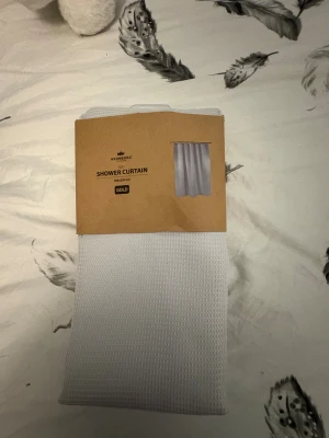 Kronborg Shower Curtain 180x200 cm Gold - Ny duschdraperi från Kronborg, modell Gold, 180x200 cm. Tillverkad av 100% polyester med vit struktur. Oöppnad förpackning, OEKO-TEX certifierad. Perfekt för att fräscha upp badrummet. Inga synliga defekter eller slitage.