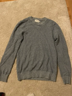 Grå stickad tröja från Easy West - En stilren grå stickad tröja från Easy West med rund hals och ribbade muddar vid ärmslut och nederkant. Perfekt för dig som gillar enkel och clean look. Långärmad och passar till många olika outfits.