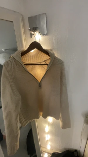 Beige stickad half zip tröja - Mysig beige stickad tröja med half zip och hög krage. Tröjan har ribbat mönster, lång ärm och en lite loose passform. Perfekt för lager-på-lager och chill dagar. Enkel att matcha med både jeans och mjukisbyxor.