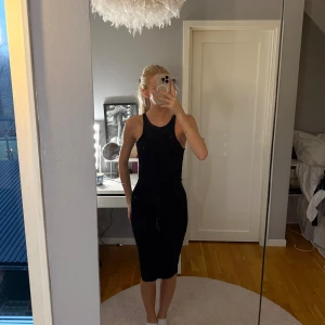 Svart ribbad midiklänning - Säljer en svart, ribbad klänning med tight passform och ärmlös design. Klänningen sitter snyggt längs kroppen. Materialet är stretchigt och bekvämt, perfekt för dig som gillar en stilren look.