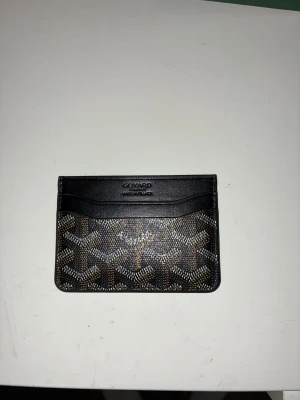 En snygg svart/brån korthållare - En väldigt stilig svart/brun korthållare med ett elegant mönster både på fram och baksida. Denna korthållare är perfekt till dig som vill ha en lite med flashig korthållare