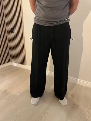 Nike tech fleece  - Svarta mjukisbyxor från Nike med breda ben och normal passform. Byxorna har snörning i midjan och raka ben, samt diskreta fickor på sidorna. Materialet är mjukt och bekvämt, perfekt för chill eller träning. Snygg och enkel design med stilren look.