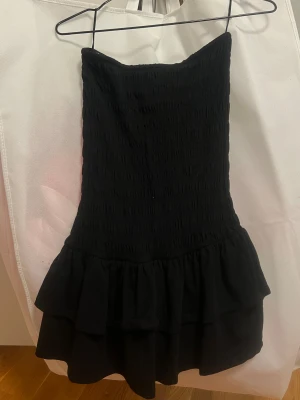 Svart axelbandslös volangklänning - Supersnygg svart axelbandslös klänning med volanger! Endast använd 1 gång💕
