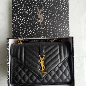 Svart quiltad  axelväska i skinn - Säljer en svart quiltad axelväska med märke Saint Laurent med ikoniskt YSL-emblem i guld framtill. Väskan är tillverkad i skinn och har en kedjerem i guldmetall. Klassisk design med lock och snygg struktur, perfekt för dig som vill ha en lyxig statementväska.