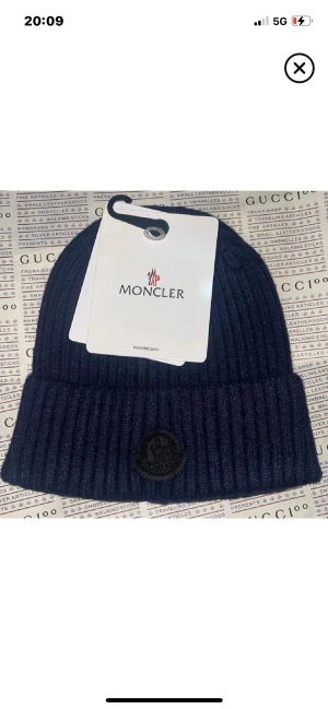 Mörkblå ribbad mössa från Moncler - Snygg mörkblå mössa från Moncler med ribbad design och uppvikt kant. Märkets svarta logopatch sitter framtill och materialet känns riktigt mjukt och varmt. Perfekt för dig som vill ha en stilren look med exklusiv känsla.