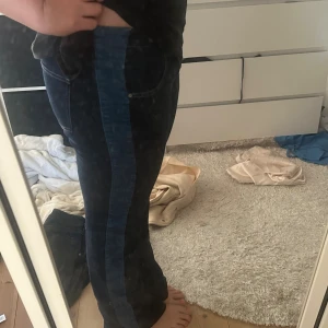 Mörkblå jeans med ljusblå sidopanel - Snygga mörkblå jeans med en bred ljusblå panel längs utsidan av benen. Klassisk femficksmodell med bootcut/raka ben och kontrastsömmar. Jeansen har normal passform och är tillverkade i jeansmaterial. Perfekt för dig som vill ha en unik twist på dina denim. Midjemått 41cm tvärsöver, innerbenslängd cirka 83cm