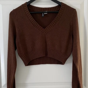 Brun croppad stickad topp H&M Divided - Säljer en brun croppad stickad topp från H&M Divided. Toppen har v-ringad hals, långa ärmar och bred ribbad kant vid nederdelen och halsen. Perfekt för dig som gillar en chill och trendig look.