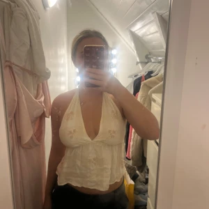 Cremefärgad  halterneck linnetopp - Supersöt vit halterneck topp i linne med broderade blommor och knyt i ryggen. Öppen i ryggen!