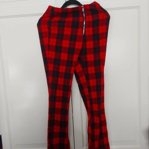 Rödrutiga byxor från H&M Divided - ⚠️ Skriv till mig innan köp! ⚠️Snygga röda och svarta rutiga byxor från H&M Divided i storlek 36. Byxorna har dragkedja framtill, bootcut-ben med slits nertill och är tillverkade i ett mjukt bomullsmaterial. Perfekta för dig som vill sticka ut med ett coolt rutmönster.