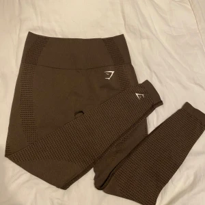 Vital seamless leggings från Gymshark - Snygga bruna leggings från Gymshark med hög midja. Stretchigt syntetmaterial som sitter tight och bekvämt, perfekt för gymmet eller annan träning. Diskret logga i vitt på benet och höften. Endast använda ett fåtal ggr! Ordinarie pris 549kr✨
