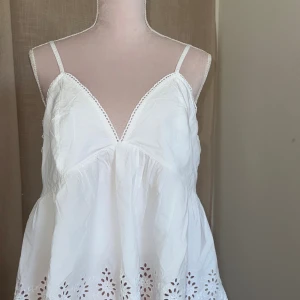 Vit topp - Superfin vit linnetopp med smala axelband och v-ringning. Toppen har broderade hålmönster längs fållen samt volangig, luftig passform. Perfekt för varma dagar och sommarvibbar. Originalpris 399kr men jag säljer för 70kr. Helt ny från bik bok. Justerbara axelband. 