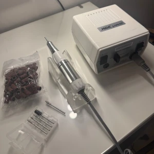 Elektrisk nagelfil med tillbehör  - Elektrisk nagelfil från Nagelgiganten. Komplett kit med kontroll enhet, hand stycke och gummiställ och fotpedal. Följer med 4 olika bitsar som kom i kitet + en extra ”hard alloy grinder, small fotball- medium” från NG, nypris: 400kr. Följer även med 80-90st slipningar, ej säker på grit men har för mig att det är 180. 