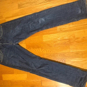 Levi's 501 Premium jeans blå W28 L32 - Klassiska Levi's 501 Premium jeans i mörkblå denim. Rak passform med fem fickor och knappgylf. Snygga kontrastsömmar och ikonisk läderpatch bak i midjan. Perfekta för dig som gillar tidlös stil och vill ha ett par jeans som funkar till allt.