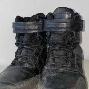 Svarta kängor från Trekmates strl 33 - Svarta kängor från Trekmates i modell SO TRIZZLER JR. Skorna har snörning, kardborreband upptill och en robust sula. Ovandelen är i skinn och textil, med vadderad insida för extra komfort. Perfekta för dig som gillar en sportig och urban look.