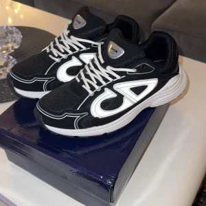 Dior B30 svarta sneakers med reflex - Säljer ett par Dior B30 sneakers i svart med vita och reflekterande detaljer. Skorna har en chunky vit sula, mesh och syntetmaterial, samt tydliga CD-loggor på sidor och häl. Klassisk snörning och sportig vibe, perfekta för dig som gillar statement sneakers.