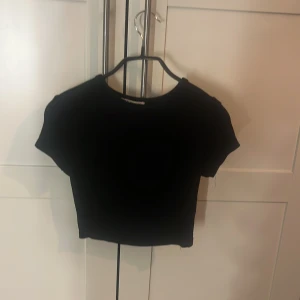 Svart croppad topp från Zara - Säljer en svart croppad topp från Zara med rund hals och korta ärmar. Enkel och stilren design som är lätt att matcha med olika outfits. Materialet känns mjukt och stretchigt, perfekt för dig som gillar en slim passform.
