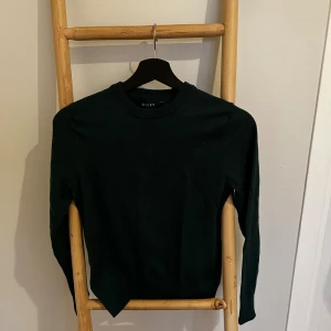 Mörkgrön merinoullströja från Riley - Snygg mörkgrön stickad tröja från Riley i mjuk merinoull. Klassisk rund halsringning och långa ärmar. Perfekt för dig som gillar stilrena och bekväma plagg med en enkel men elegant look. Tröjan är ursprungligen S men krymptes i masken så passar nu XS