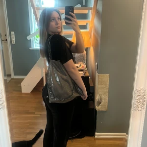 Silver väska - Säljer en snygg grå axelväska vintage men liknar en Stella McCartney med glansig silver yta med silver kedjor och ett litet innerfack oxå. Säljer pågrund av ingen användning längre 