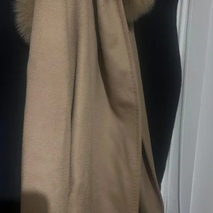 Beige kappa med päls MaxMara - Säljer en beige kappa från MaxMara med stor fluffig päls runt kragen. Kappan har en klassisk rak passform och är tillverkad i ett mjukt material som känns lyxigt. Perfekt för dig som vill ha en elegant och tidlös look. Priset kan diskuteras 