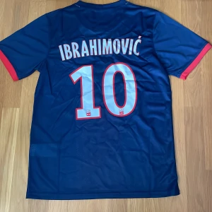 PSG  2014/2015 Ibrahimovic 10 Nike fotbollströja S - Paris Saint-Germain matchtröja med Ibrahimovic 10 på ryggen. Klassisk design i mörkblått med röd mittremsa, vita detaljer och röda ärmslut. Tillverkad i Dri-FIT material som andas. PSG-emblem och Fly Emirates-tryck på bröstet.