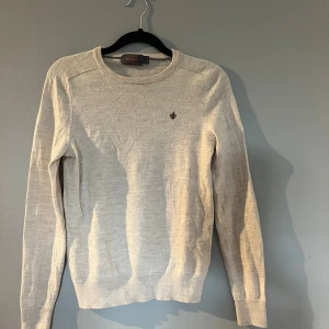 MORRIS TRÖJA  - Ljusbeige rundhalsad tröja från Morris i 100% merinoull. Stilren design med diskret broderad logga på bröstet och ribbade muddar vid ärmslut och nederkant. Perfekt för dig som gillar klassisk och enkel stil. Jag är 160 cm lång och uppskattar att tröjan passar dem som har 150-155 i storlek. Den är tvättad en gång och har därför krympt lite varför jag har en bild på mig med tröjan så att ni förstår hur stor/liten den är. Mycket skön och stilren ulltröja.