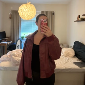 Vinröd skinnjacka från LXA - Säljer en vinröd skinnjacka från LXA i storlek 34. Jackan har bred krage, dragkedja framtill och ribbade muddar vid ärmslut och midja. Oversized passform och klassisk bomberstil som ger en cool vibe till din outfit.