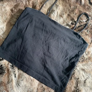 Svart enkel crop top med smala band - Säljer en svart, stilren crop top  med smala axelband.