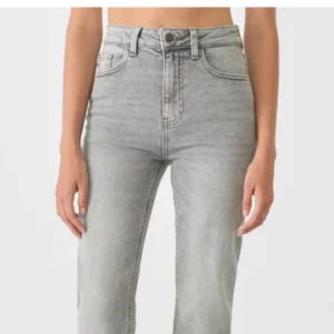 Grå raka jeans från STR Teen - Snygga ljusgrå jeans från STR Teen med hög midja och raka ben. Klassisk femficksmodell med dragkedja och knapp framtill. Jeansen är tillverkade i ett mjukt denimtyg som ger en avslappnad och trendig look.