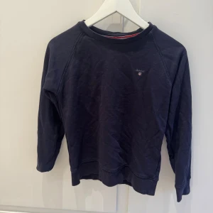 Mörkblå sweatshirt från Gant - En klassisk mörkblå sweatshirt från Gant med broderad logga på bröstet. Tröjan har rund halsringning, ribbade muddar och är tillverkad i mjuk bomull. Perfekt för en avslappnad och stilren look.
