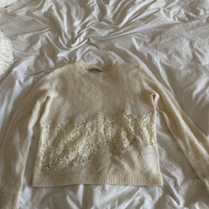 Beige stickad tröja med spets från Zara - Superfin beige stickad tröja från Zara med bred spetsdetalj i blommigt mönster över magen och ryggen. Tröjan har rund halsringning och långa ärmar, perfekt för dig som gillar romantiska detaljer och mjuka material.