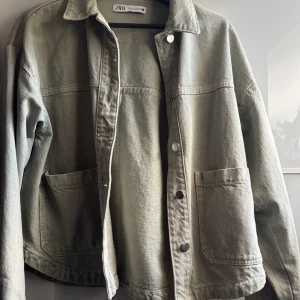 Grön jeansjacka från Zara XS - Snygg grön jeansjacka från Zara i storlek XS. Jackan har klassisk krage, stora framfickor och knäppning med silvriga knappar. Rak passform och lång ärm, perfekt för lager-på-lager. Materialet är kraftigt och ger en cool, avslappnad vibe.