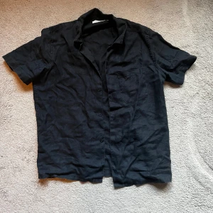 Linneskjorta från samsøe - Svart kortärmad skjorta från Samsøe Samsøe i luftig linnekvalitet. Klassisk krage, knäppning framtill och bröstficka. Perfekt för en clean och avslappnad stil.