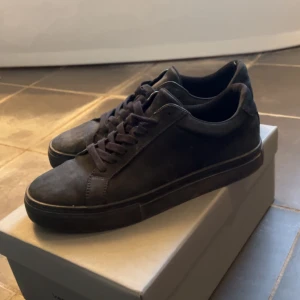 Svarta sneakers från Vagabond i mocka - Stilrena svarta sneakers från Vagabond i mocka med klassisk låg profil och rund tå. Skorna har snörning och platt sula, perfekt för en clean och enkel look. Diskret branding på insidan och baksidan. Passar till det mesta och ger en snygg vibe.Går att rengöra för att få dem att se bättre ut men inget jag kommer göra.Storlek 41.Kan inte ge en bild med de på för att de är för små.Har ni frågor eller funderingar skriv till mig😃