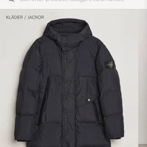 Svart pufferjacka från Stone Island - Säljer en svart pufferjacka från Stone Island med huva och klassisk logotyp på ärmen. Jackan har dragkedja, stora fickor och quiltad design. Perfekt för kalla dagar och riktigt snygg streetstil.