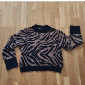 Stickad tröja - Säljer en stickad tröja från H&M i storlek S med snyggt zebramönster. Tröjan har lång ärm, ribbade muddar och en lite högre hals.